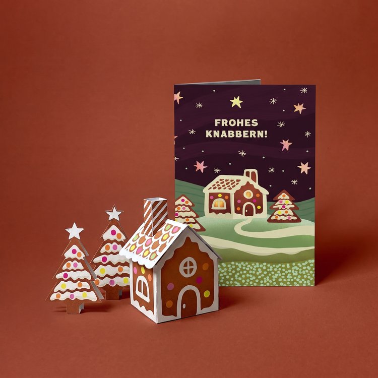 Compositing-Mockup der Faltmeister-Weihnachtskarte Lebkuchenhaus: Karte, Papierhaus und Lebkuchenbäume.